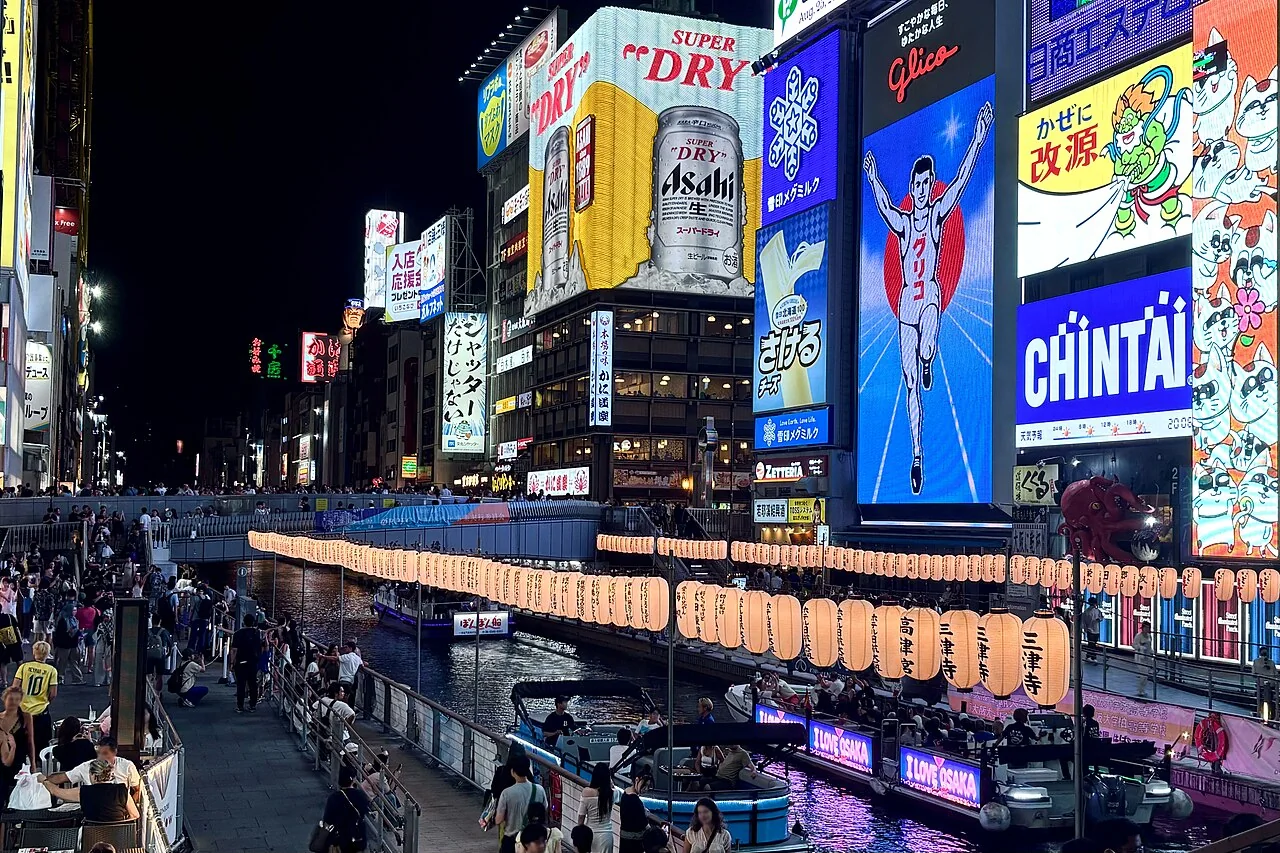 Canal de Dotonbori à noite com os letreiros da Glico e outros anúncios refletidos na água.