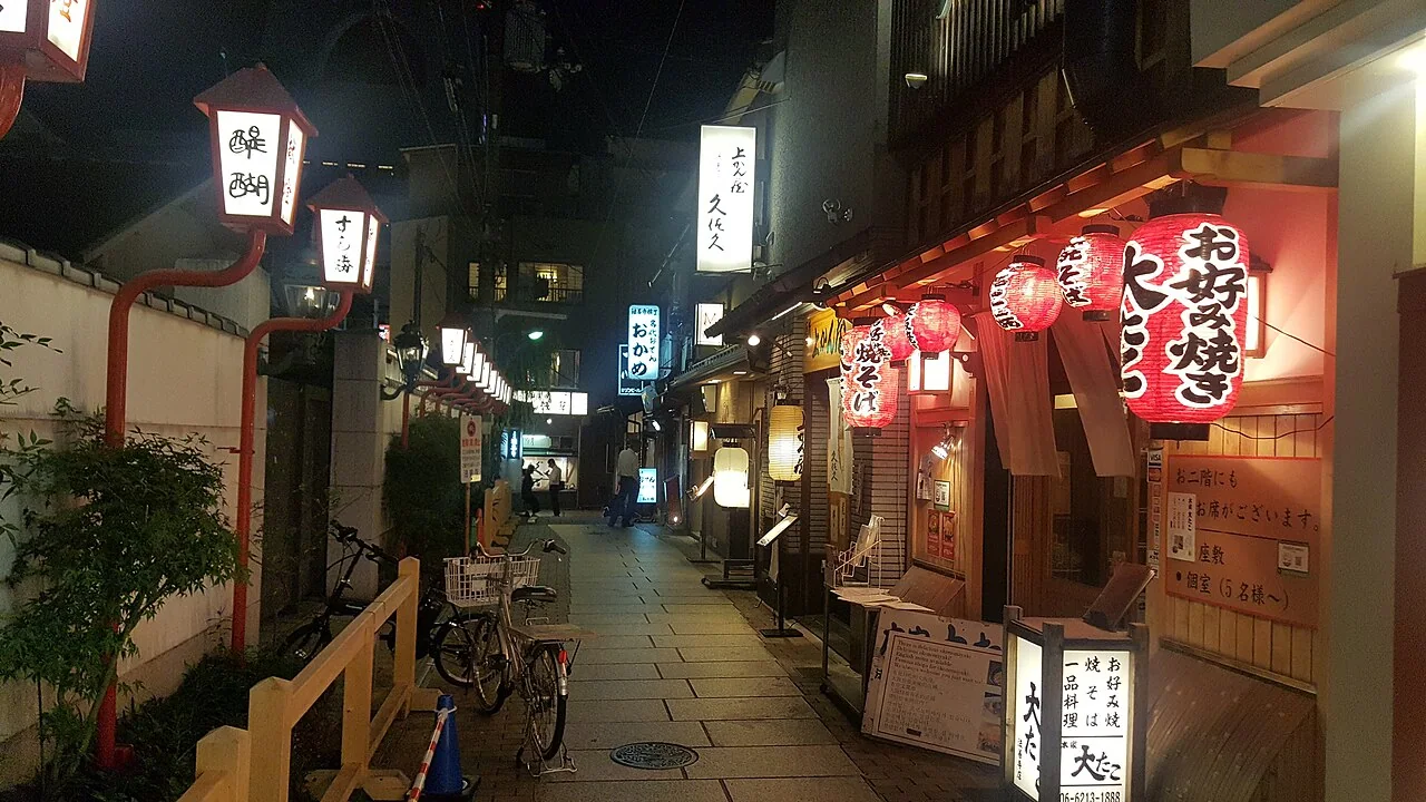 Viela de Hozenji Yokocho à noite, com restaurantes e lanternas acesas.