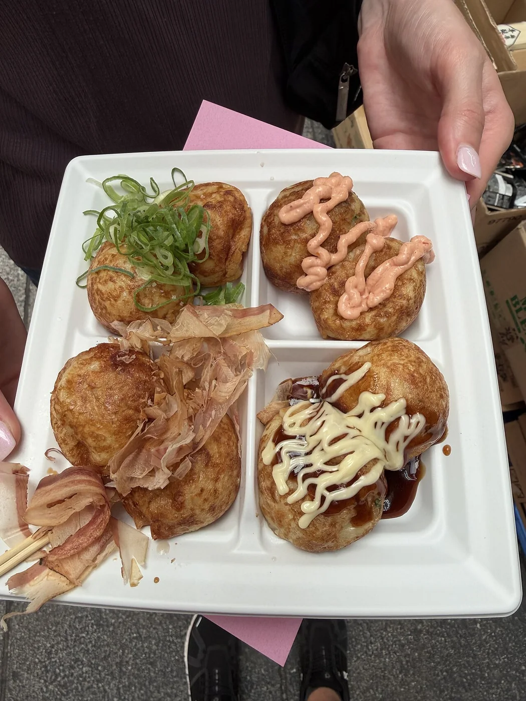 Porção de takoyaki com diferentes coberturas em prato dividido.