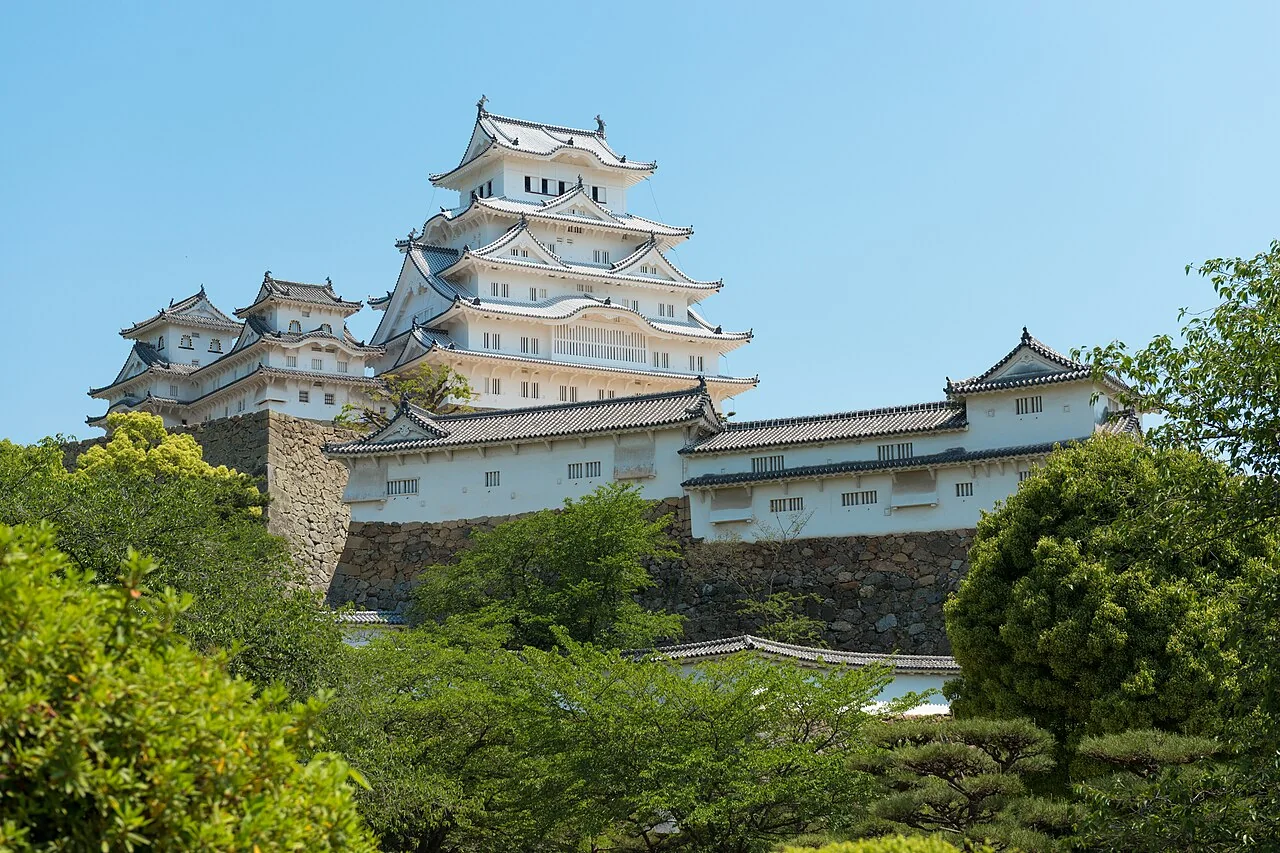 Castelo de Himeji com paredes brancas e telhados sobrepostos acima da vegetação.