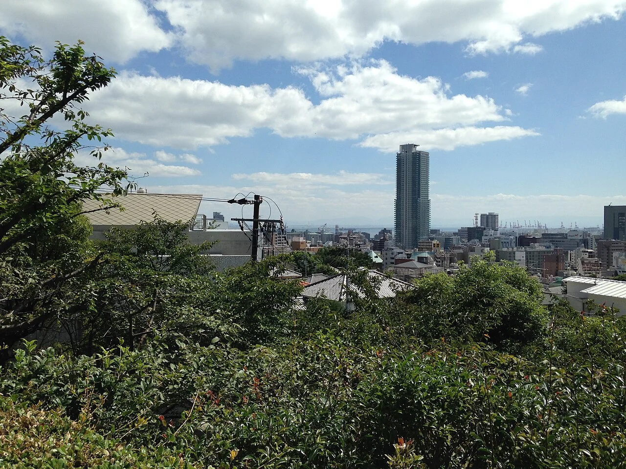 Vista de Kobe a partir do Santuário Kitano Tenman, com vegetação e edifícios ao fundo.