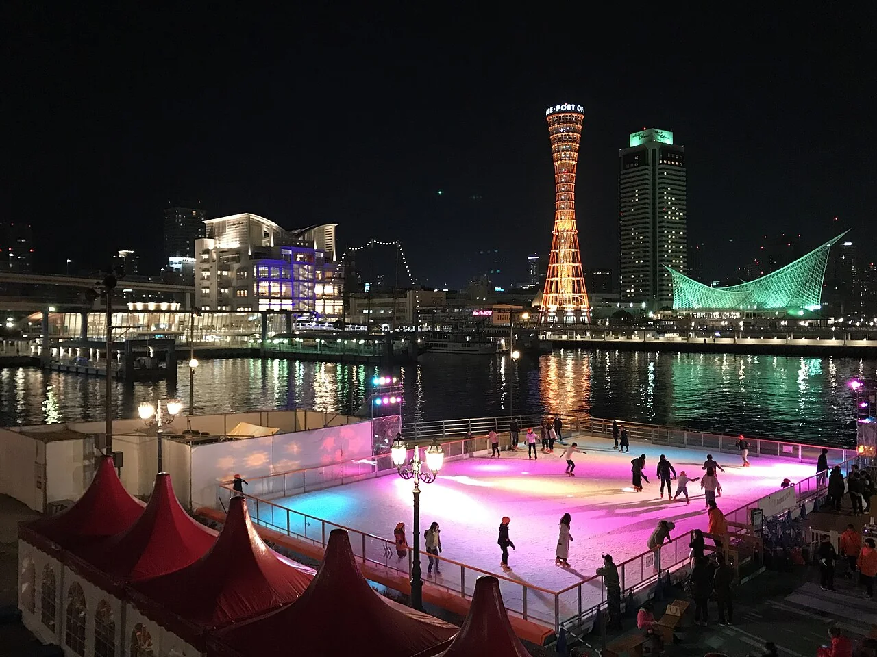 Torre do porto de Kobe e orla iluminada à noite, com instalação de patinação em primeiro plano.