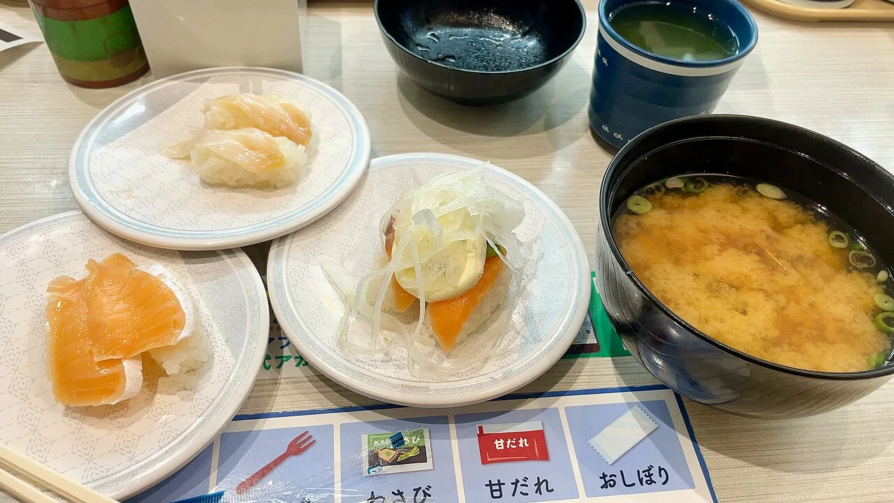Três pratos de sushi e uma tigela de missoshiru sobre uma mesa do Hama-sushi.
