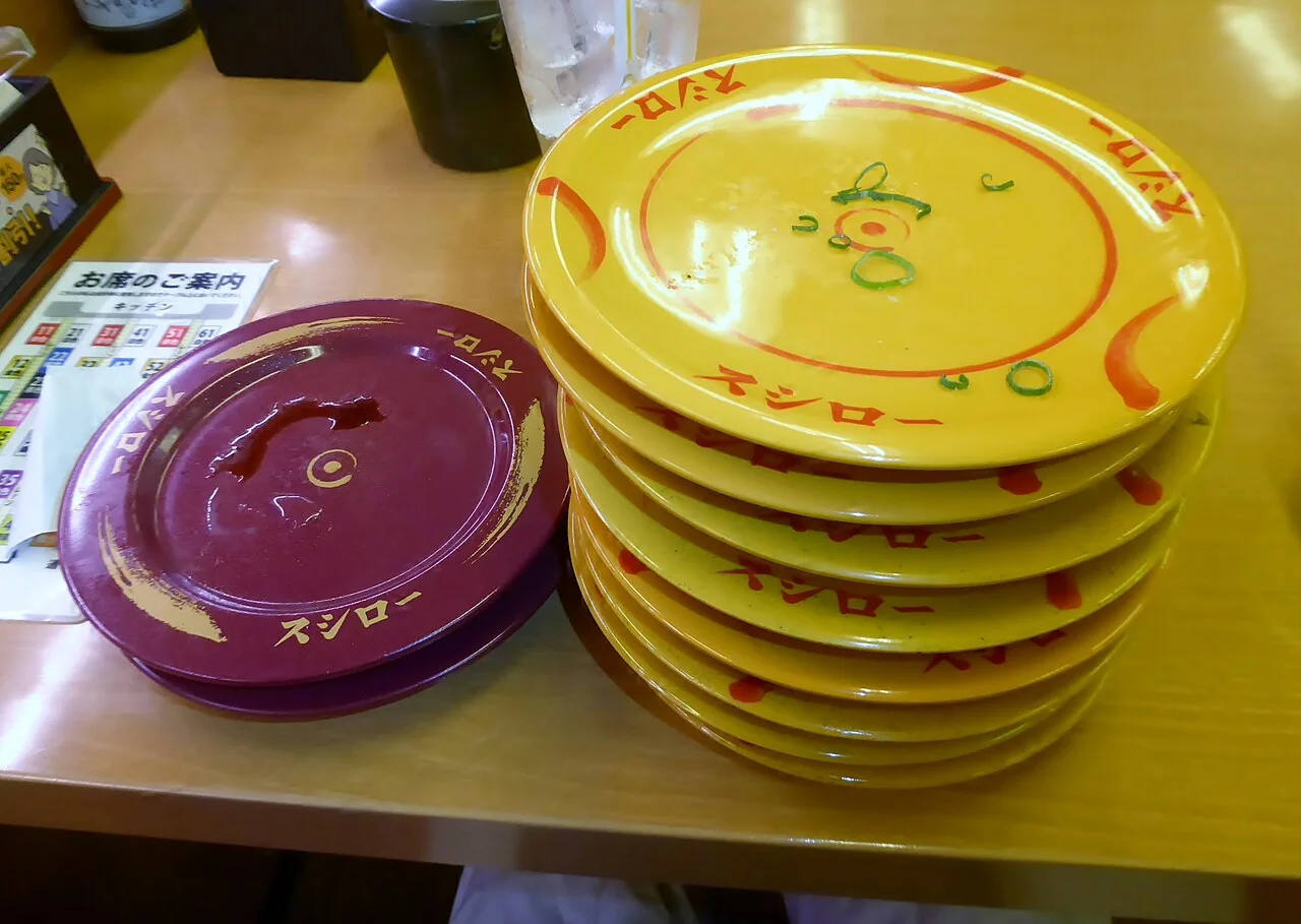 Pratos vazios de diferentes cores, com uma pilha de pratos amarelos, no Sushiro.
