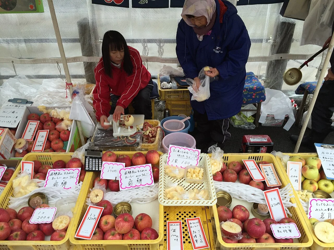 Visitantes diante de uma banca de frutas no mercado da manhã Miyagawa, em Takayama.